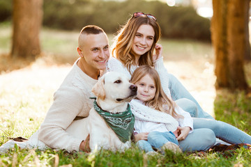 Fototapeta premium Happy beautiful family with dog labrador is having fun are sitting on green grass in park.
