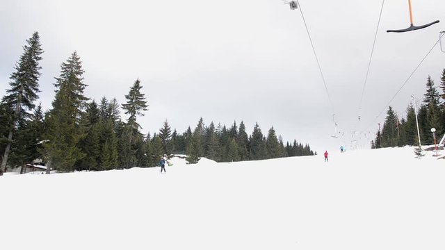 Skiers using ski lift anchor on the mountain. People moving slowly uphill on drag lift on snow covered landscape. Winter sports, skiing, recreation and holidays concept. 