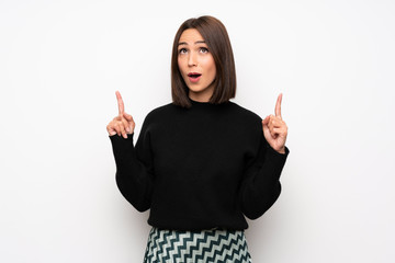 Young woman over white wall pointing up and surprised