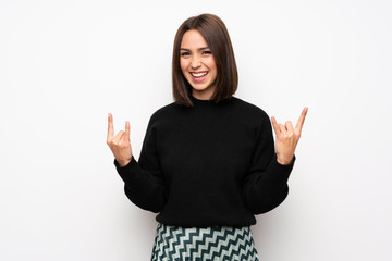 Young woman over white wall making rock gesture