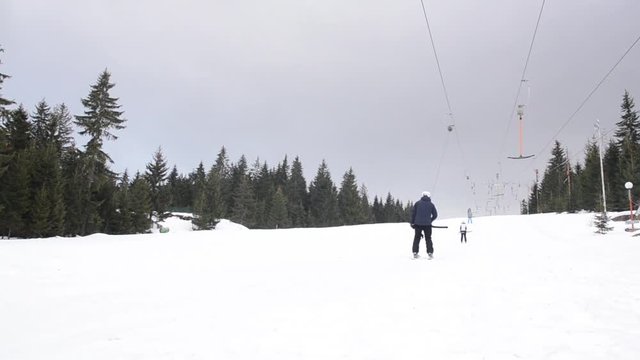Skiers using ski lift anchor on the mountain. People moving slowly uphill on drag lift on snow covered landscape. Winter sports, skiing, recreation and holidays concept. 