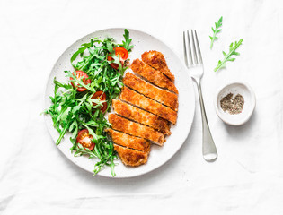 Traditional chicken schnitzel with arugula cherry tomatoes salad on light background, top view