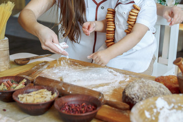 child with his mother in the kitchen sprinkles flour dough. Products from dough, flour, bakery, bread. Master Class. cook and learn
