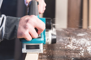 The hands of a carpenter working woodworking power tools. Close up of the work of the electric planer