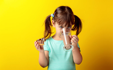 Four-year-old girl in a turquoise t-shirt eat donuts and drink chocolate milk.