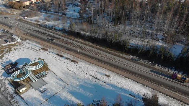 Panning and tilting drone footage showing a road with cars driving nearby a blue infinity shaped water slide on a beautiful cold sunny winter day in Sweden. Filmed in realtime at 4k.