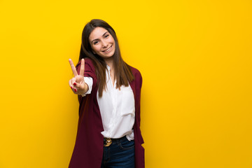 Young woman over yellow wall smiling and showing victory sign