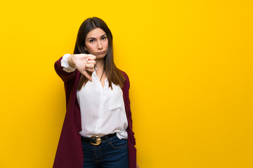 Young woman over yellow wall showing thumb down with negative expression