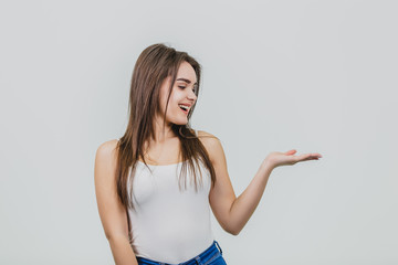 Fototapeta na wymiar A young pretty Caucasian girl stood on a white background. During this time wear a white T-shirt and blue jeans. Turning his hand to the side looks at her.