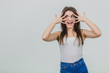 A pretty young girl standing on a white background. The girl is dressed in a white shirt. Has beautiful black long hair. Having put all the fingers of two hands, the elongated girl puts them on the