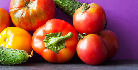 Organic vegetables harvest on purple black background. Ripe bell pepper, yellow red tomatoes cucumbers. Close-up photo.