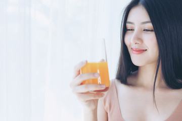 Beautiful beauty woman Asian cute girl feel happy drinking orange juice for good health in the morning , enjoying time in her home  white bedroom background - lifestyle beauty woman concept