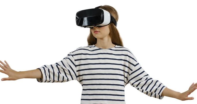 Teenage girl with long hair, in VR glasses and striped blouse having VR headset while standing on the white wall background.