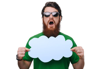 Photo of amazed beardd man wearing sunglasses, and green tshirt holding a speech cloud