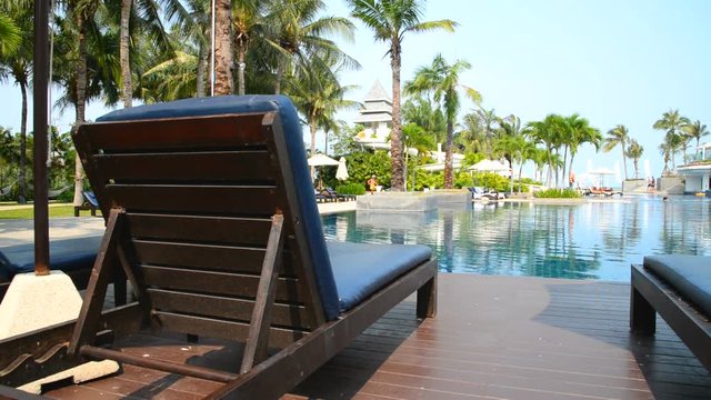 A deck chair overlooks a beautiful pool at a luxurious tropical resort.