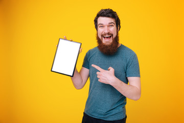 Photo of happy smiling  bearded man pointing at white screen of tablet while looking at camera