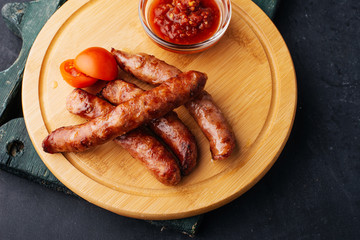 Grilled sausages with sauce ketchup and tomatoes on a wooden plate