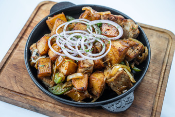 Fried potatoes with meat, broccoli and red onions decorated with rosemary in a frying pan on a wooden table top view