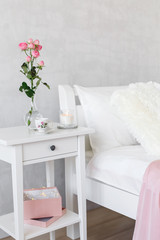 Fototapeta na wymiar Light female modern stylish and cozy bedroom. Bed with white linen, bedside table, vase with rose flowers, lighted candle, cup of tea.
