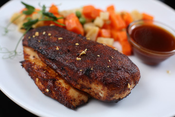 chicken fillet, baked with spices and covered with an appetizing crust, on a plate with vegetables and sauce