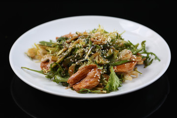 salad of a large amount of greens, green celery, arugula, boiled meat fillet with sauce and sesame