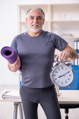 White bearded old man employee doing exercises in the office 