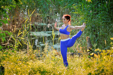 Young woman practicing yoga pose against a background of green nature in the forest