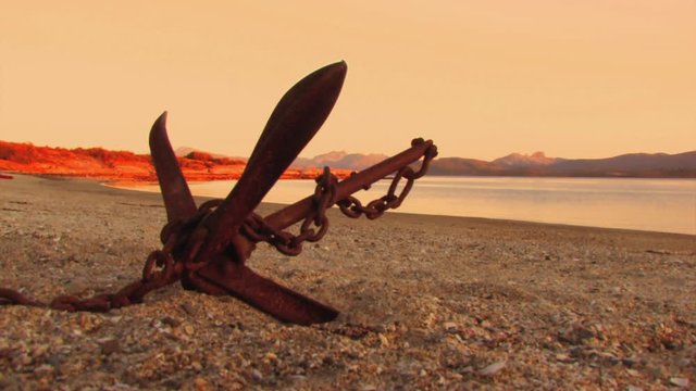 View of the coast with a corroded metal anchor in the foreground, mountains in the background of the scene