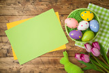 Easter holiday background with paper note, easter eggs in basket and tulip flowers on wooden table.