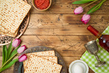 Jewish holiday Passover background with matzo, seder plate, wine and tulip flowers on wooden table.