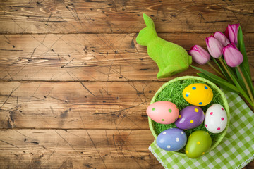 Easter holiday background with easter eggs in basket and tulip flowers on wooden table.