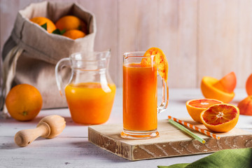 Glass of fresh pressed orange juice and blood oranges on wooden table. Bright summer mood. Top view