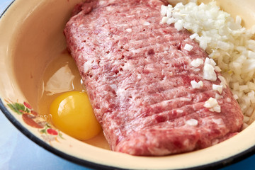 fresh beef and pork minced meat sprinkled with white onions and chicken egg for making cutlets and schnitzel in a yellow iron plate. twisted meat in a meat grinder