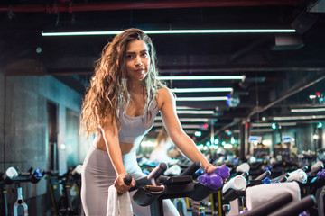 Naklejka na ściany i meble Beautiful young woman exercising on cycling machine in the gym