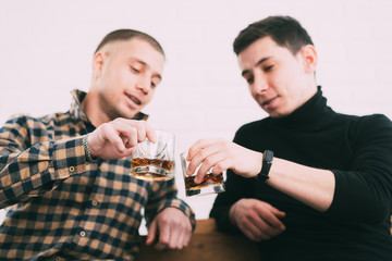 two men drink whiskey sitting on a wooden couch