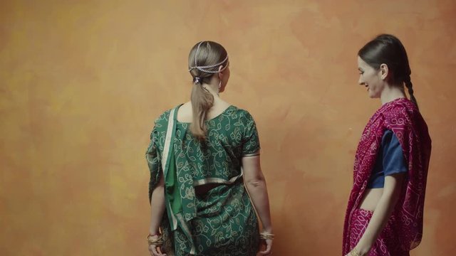 Two charming women in colorful traditional indian clothing saree with bindi points, many bracelets and tika decoration ready for hindu initiation ceremony. Caring female finally looking at friend.