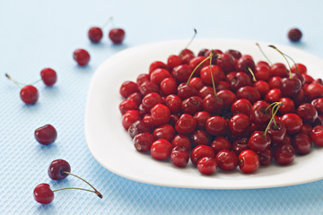 Cherry on a white plate on a blue background. Summer berries. Cherry spread out on a light background