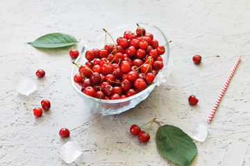 Cherry berries with leaves in a glass bowl on a gray background. View from above