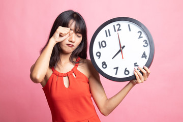 Sleepy young Asian woman with a clock in the morning.