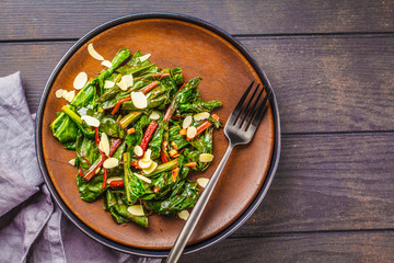 Beet greens salad with nuts in black plate, top view. Healthy vegan food concept.