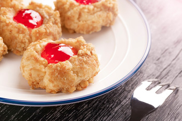 Cookies made from hazelnut shortcake with strawberry jam inside on a white plate with a patterned dessert fork.