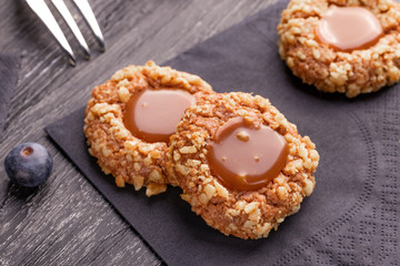 Peanut shortbread cookies with caramel jam inside on a black napkin with blueberries and a...