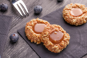 Peanut shortbread cookies with caramel jam inside on a black napkin with blueberries and a patterned dessert fork.