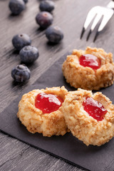 Cookies made from hazelnut shortcake with strawberry jam inside on a black napkin with blueberries