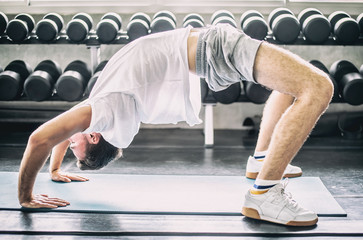 man practicing yoga bridge pose with sun light from window in gym