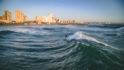 Surfer with city in background  - obrazy, fototapety, plakaty