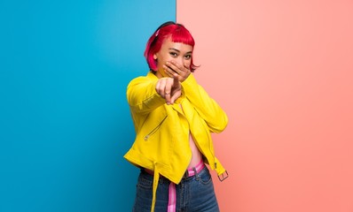 Young woman with yellow jacket pointing with finger at someone and laughing