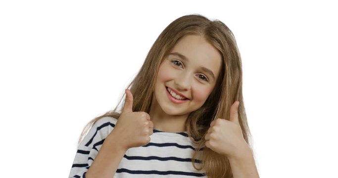 Close up of the blond pretty teen girl with long hair in the striped blouse giving her thumbs up and smiling while standing on the white wall background. Portrait