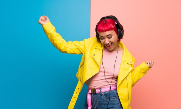 Young woman with yellow jacket listening to music with headphones and dancing
