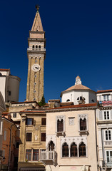 Fototapeta premium Bell and clock tower of St George's Parish Catholic Cathedral and baptistery with pink Venetian House in Tartini Square Piran Slovenia